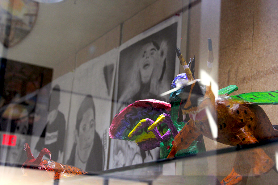 Alebrijes and charcoal self-portraits displayed in the Fine Arts Hall building.