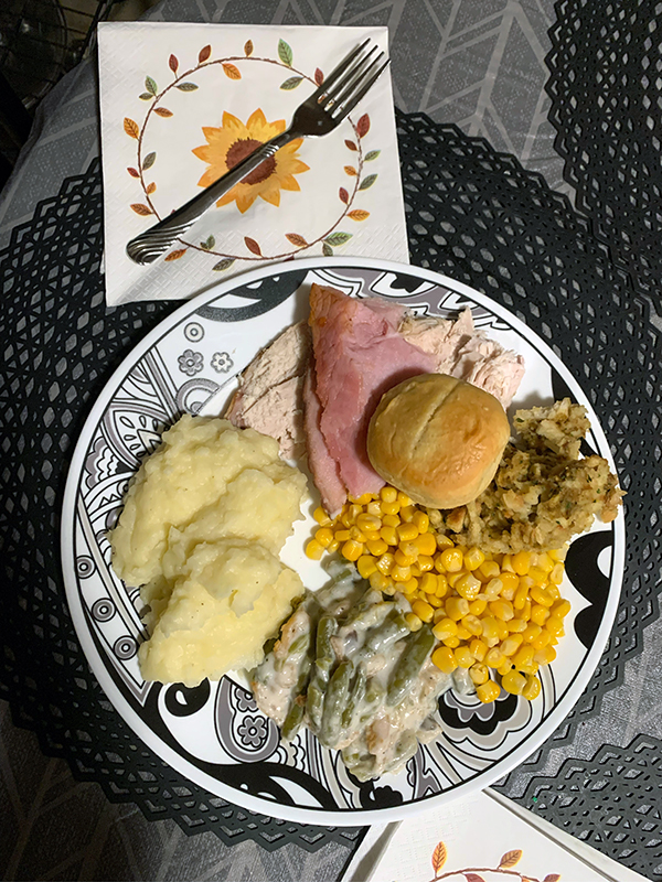 Thanksgiving dinner with traditional sides such as mash potatoes, green bean casserole, corn, stuffing, and a bread roll ready to be enjoyed. 